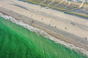 An aerial view of a beach with clear turquoise water, a sandy shore, and scattered people.