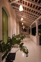Un pasillo con columnas blancas, puertas verdes y lámparas colgantes.