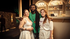 Three people standing in front of a bar area with shelves of bottles. - Cali Stays & Cafe By the Bay (Vagator)