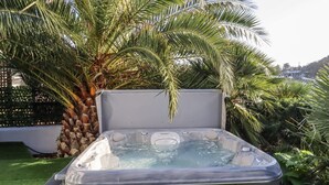 Ett bubbelbad med klart vatten, omgivet av frodig grönska och en palm.