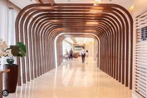 A modern hotel corridor with a curved wooden partition, a polished floor, and a reception area with a potted plant.