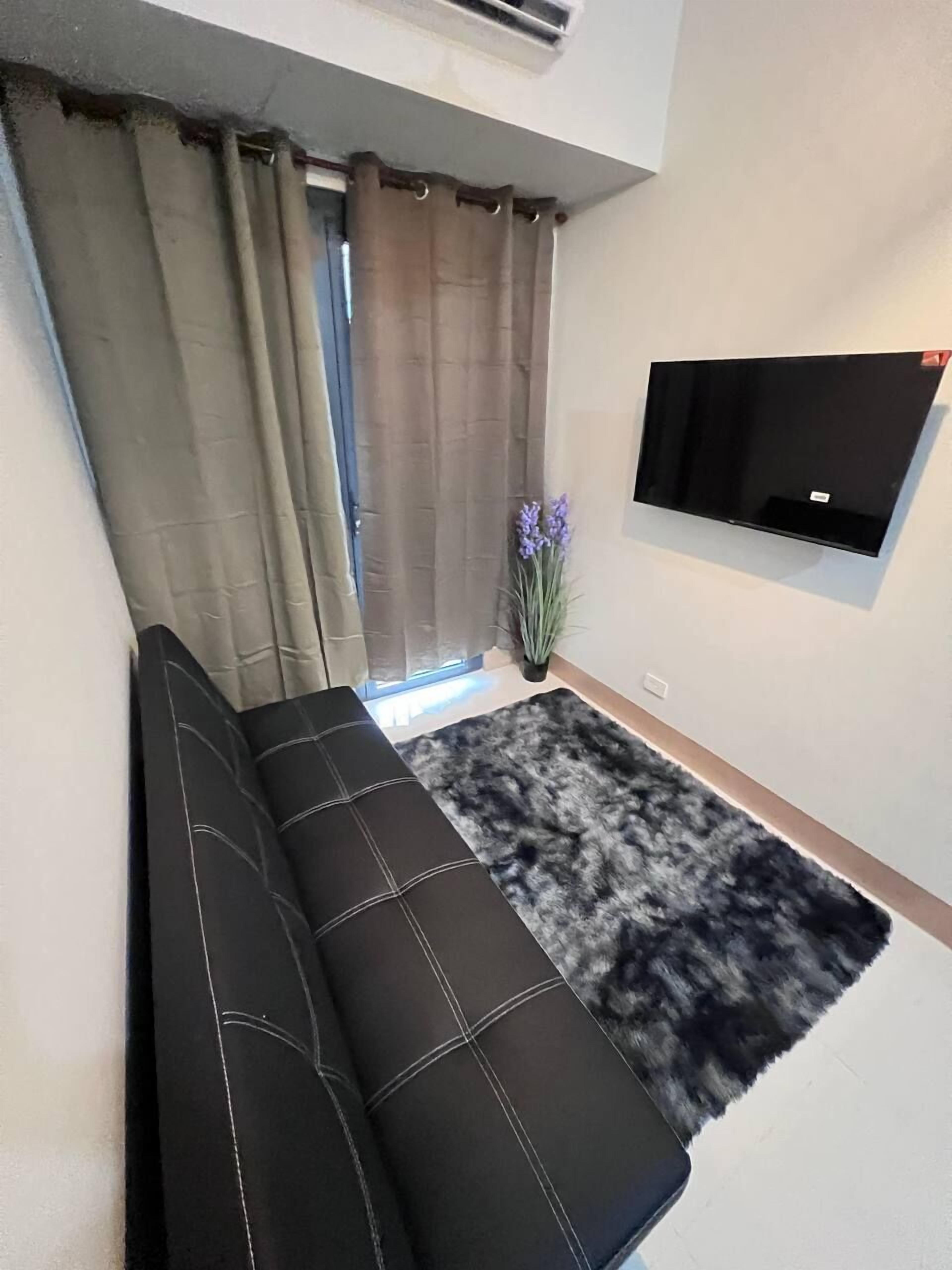 A modern living room with a black sofa, a mounted TV, and a window with curtains.