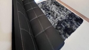Ein modernes Wohnzimmer mit einer schwarzen Couch, einem Wand-Fernseher und einem Fenster mit Vorhängen.