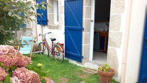 Uma casa pequena com persianas azuis, uma bicicleta e um jardim com hortênsias.