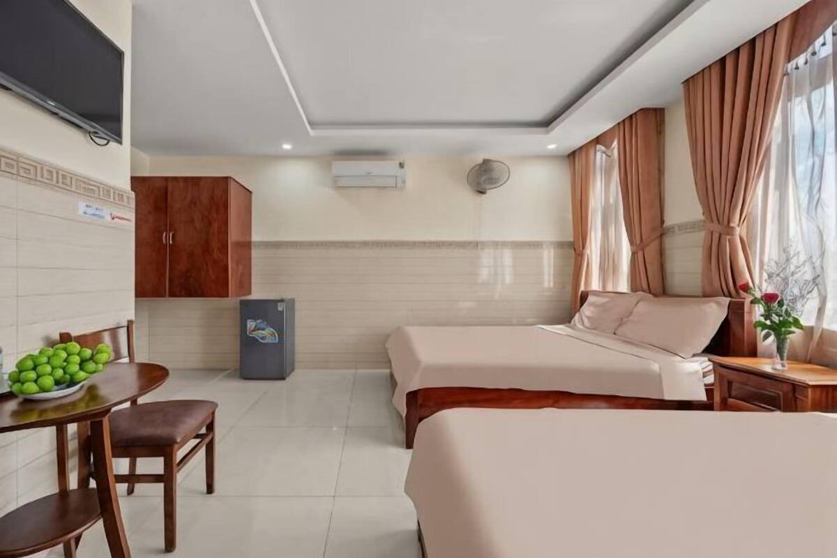 Una camera d'albergo con due letti, un tavolo da pranzo con sedie, un frigorifero e una televisione a parete.