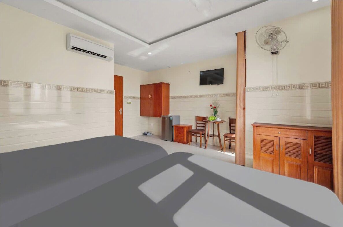 A hotel room with a bed, a small kitchenette, a TV, and a fan.