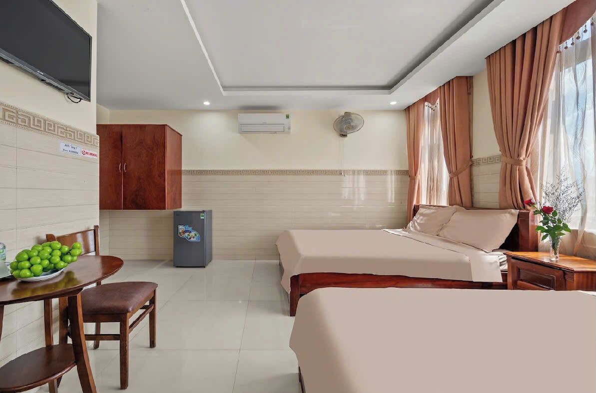 A hotel room with two beds, a dining area with a table and chairs, a TV, an air conditioner, and a refrigerator.