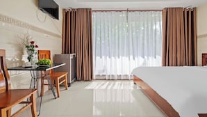 A hotel room with a bed, a desk with a chair, a small refrigerator, and a window with curtains. - BEAR HOTEL & HOMESTAY  (Da Nang)