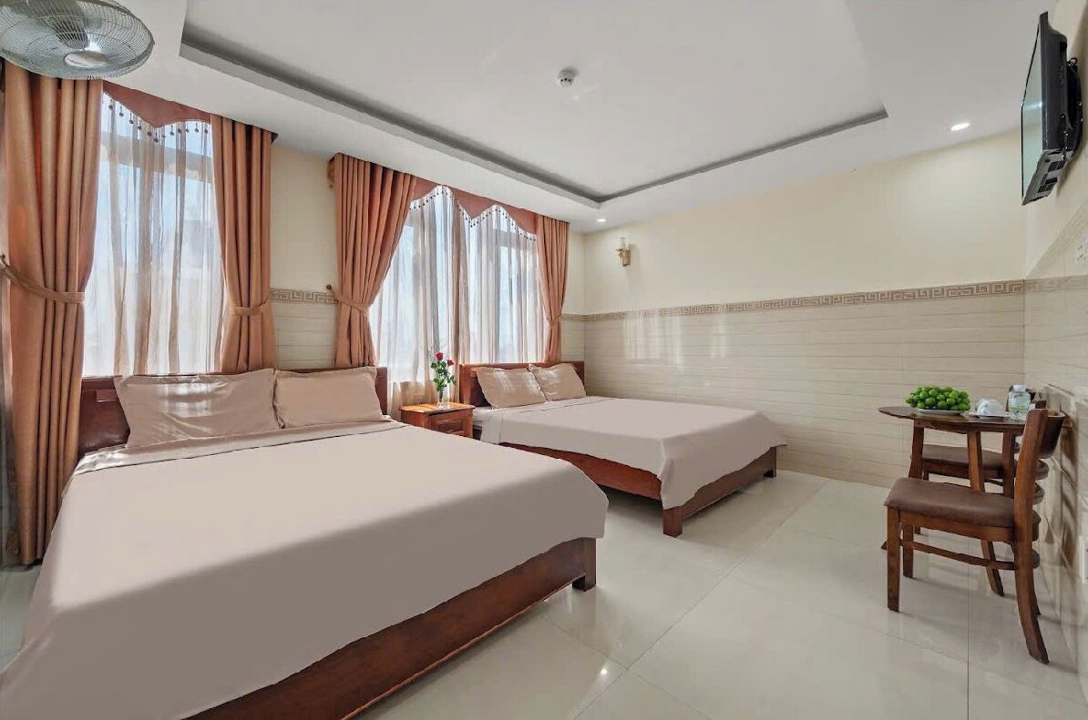 A hotel room with two beds, a dining table, and a TV mounted on the wall.