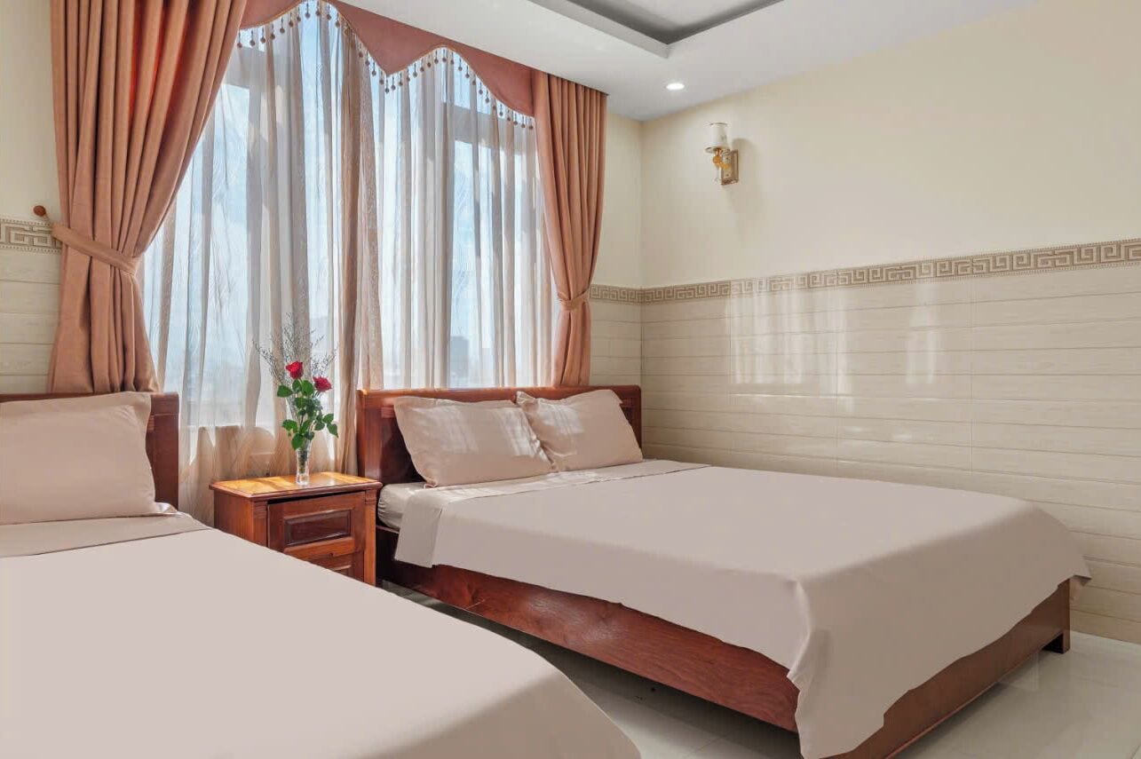 Une chambre d’hôtel avec deux lits, une table de chevet ornée d’un vase de fleurs et une fenêtre avec des rideaux.