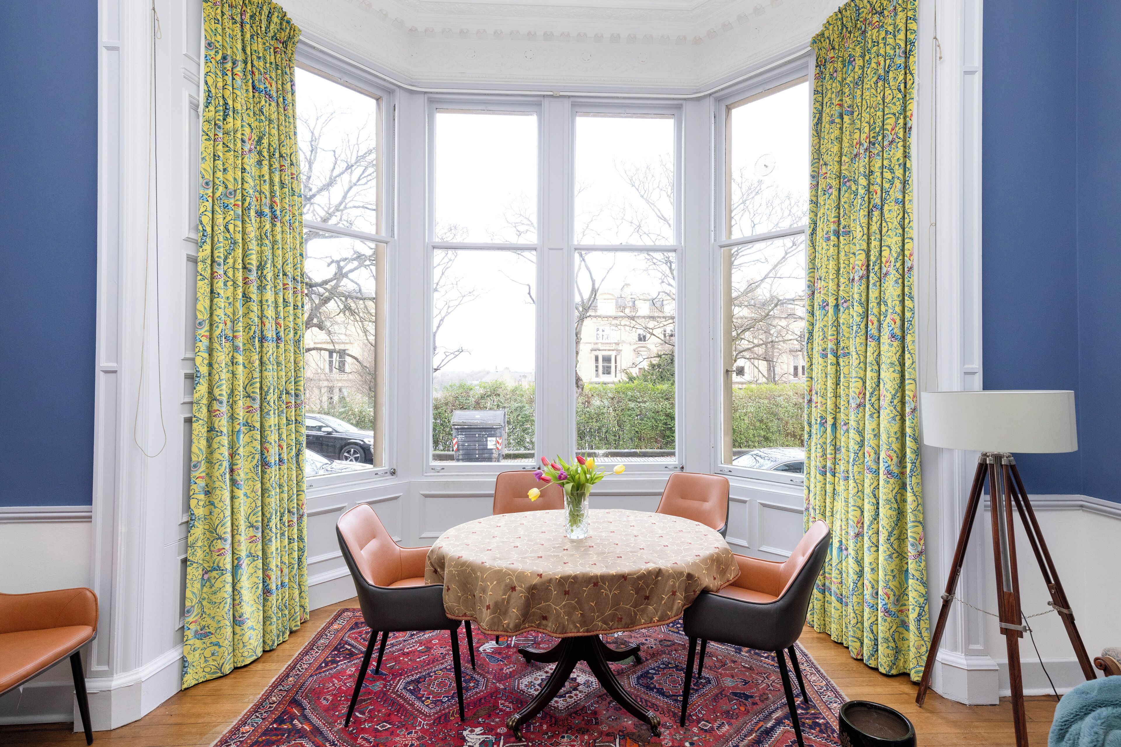 A dining area with a round table, four chairs, a vase with flowers, and a lamp.
