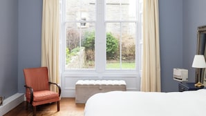 Ett hotellrum med ett stort fönster, en säng, en stol, ett sängbord med en lampa och ett element.
