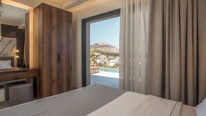 A bedroom with a bed, a wooden wardrobe, a desk with a mirror, and a view of a pool and mountain.