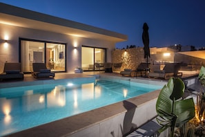 Ein moderner Poolbereich mit klarem Pool, Liegestühlen und einer Steinmauer.