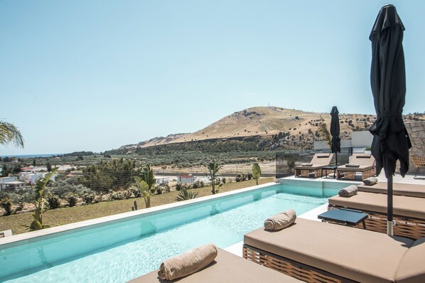 Ein Pool mit Liegestühlen und Sonnenschirmen, eingebettet in eine hügelige Landschaft.