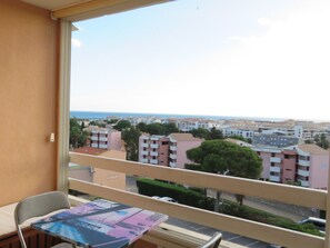A balcony with a view of a coastal town, a chair, and a table with a magazine.