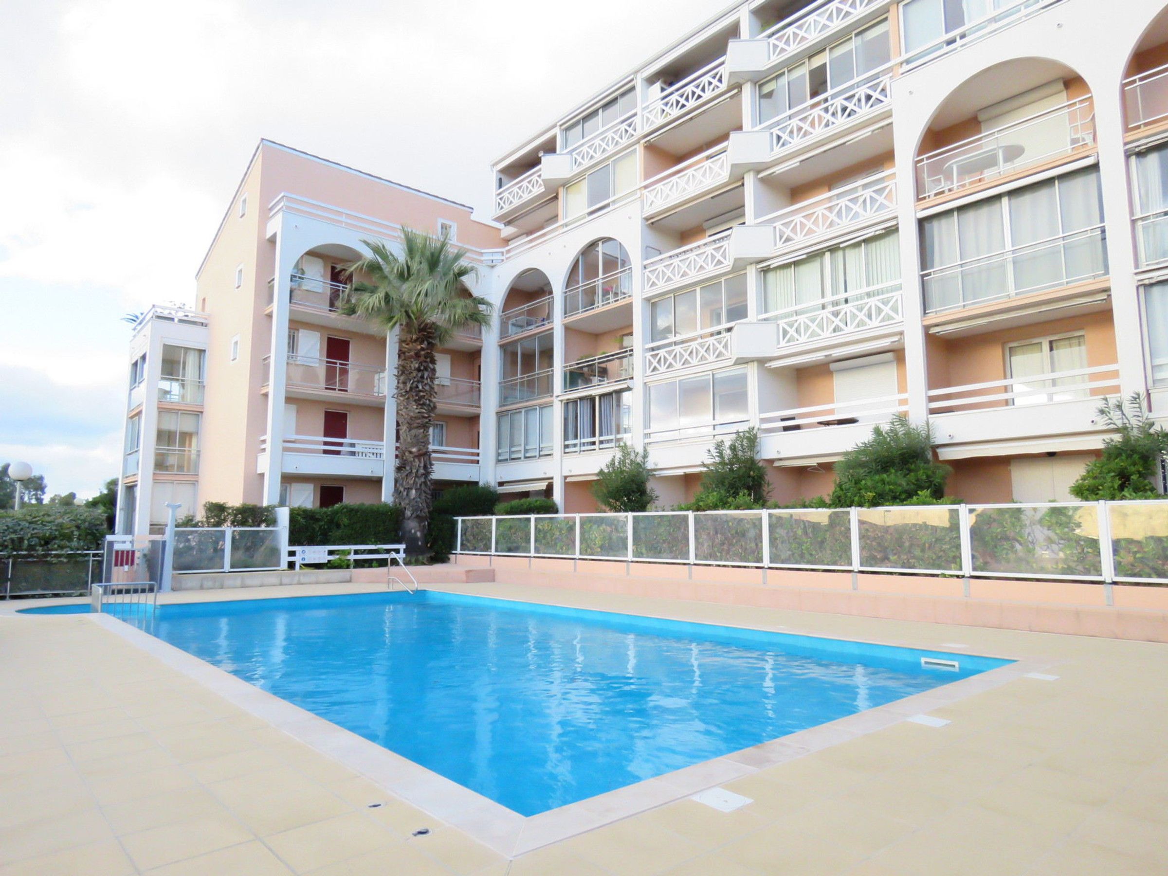 A multi-story hotel with a swimming pool, balconies, and a palm tree.