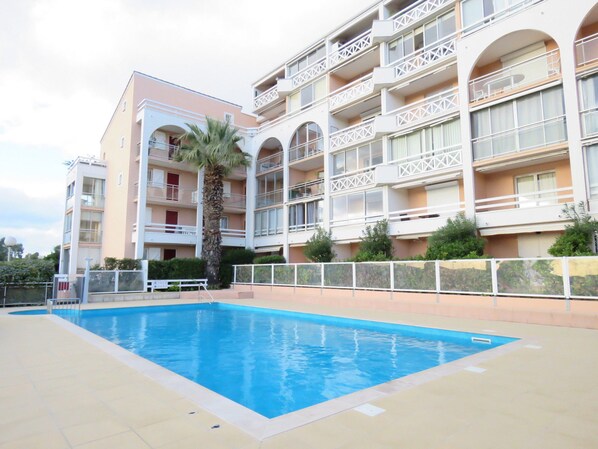 A multi-story hotel with a swimming pool, balconies, and a palm tree.