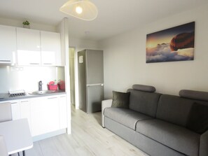 A modern kitchen with white cabinets, a grey sofa, and a painting of a landscape.
