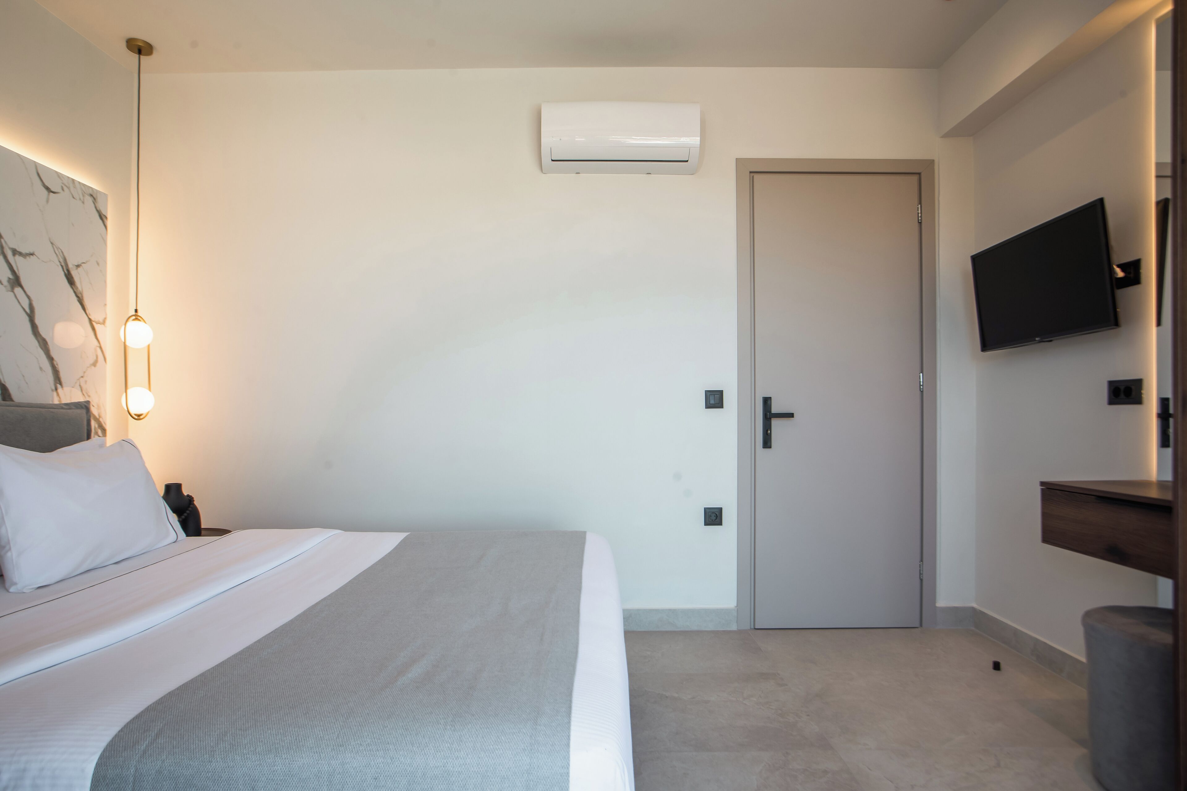 A hotel room with a bed, a wall-mounted TV, an air conditioning unit, and a door.