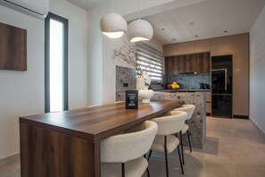 A modern kitchen with a wooden island, bar stools, pendant lights, and a stone backsplash.
