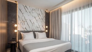 A modern hotel room with a large bed, marble wall, and a view through sheer curtains.