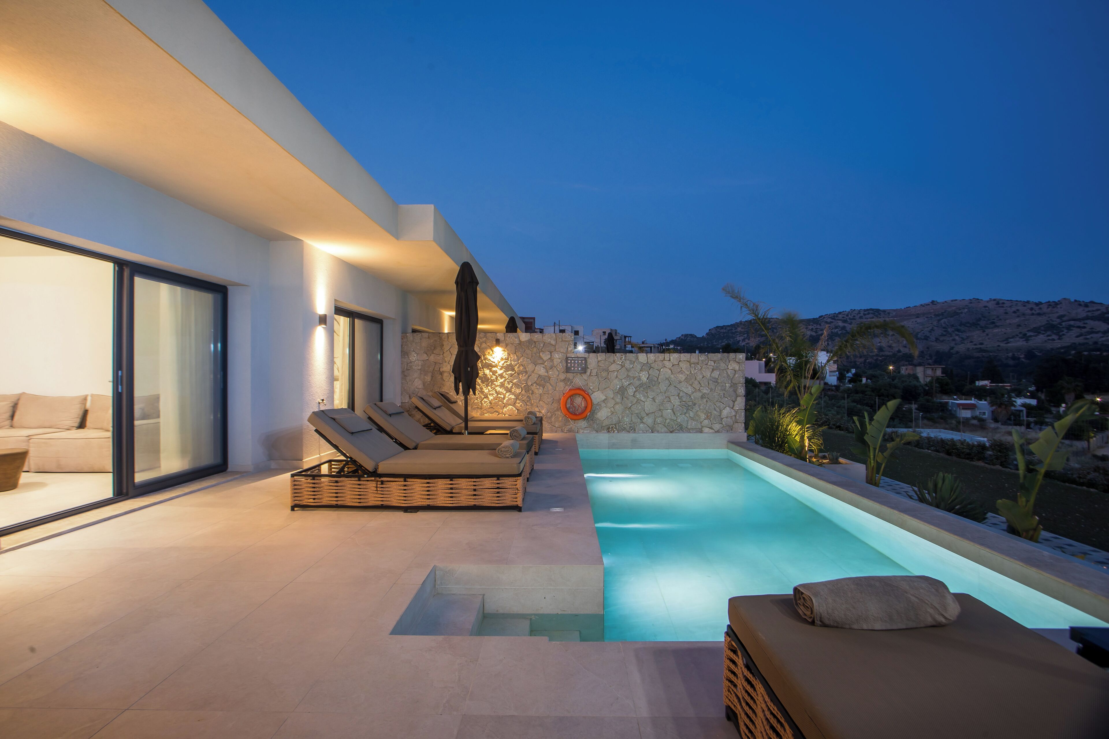 Un espace piscine extérieur moderne, doté de chaises longues, d’un mur en pierre et offrant une vue sur le paysage.