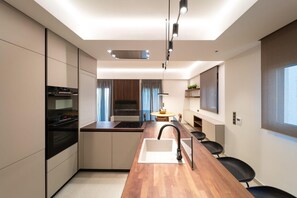 A modern kitchen with a central island, built-in appliances, and a dining area with chairs. - Kyma Luxury Apartment (Ρόδος)