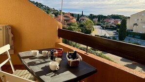Un balcone con un tavolo apparecchiato per due persone, una sedia e vista su un quartiere residenziale.