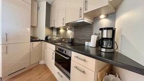 Una cucina moderna con mobili bianchi, un piano di lavoro nero, una macchina da caffè in acciaio inossidabile e un forno integrato.