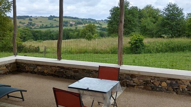 Un espacio al aire libre cubierto con una mesa y sillas, paredes de piedra y vistas a un paisaje verde.