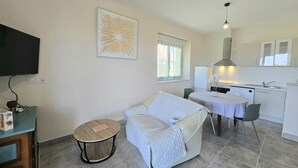 Habitación pequeña con cama, una mesita redonda, kitchenette y televisor fijado en la pared.