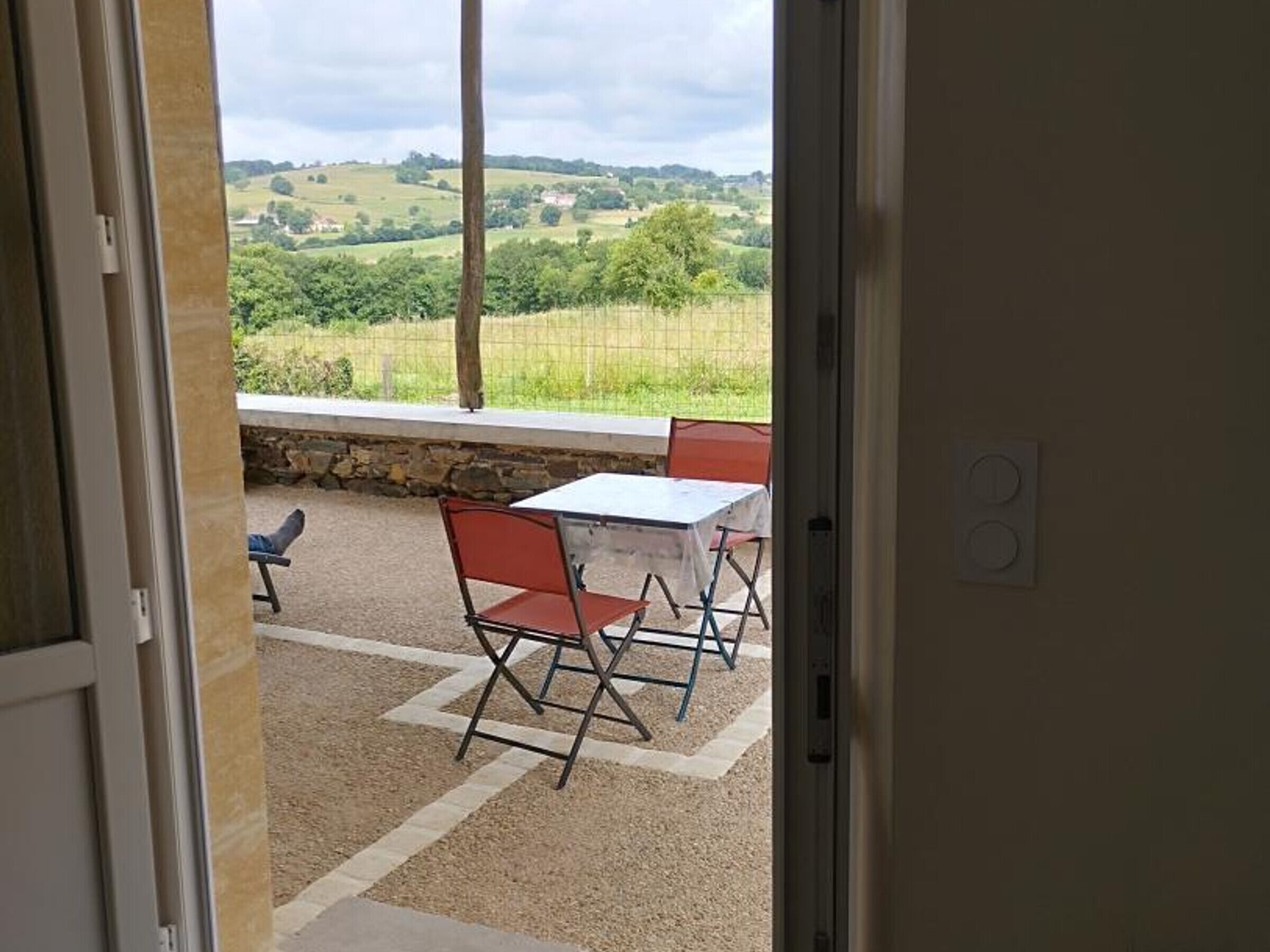 A patio with a table and chairs, a stone wall, and a view of a green landscape.