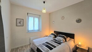Un dormitorio con cama, mesita de noche, lámpara colgante, ventana con cortinas e imagen enmarcada en la pared.