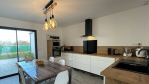 Una cocina moderna con zona de comedor, que incluye una mesa de madera, sillas blancas y un horno empotrado.