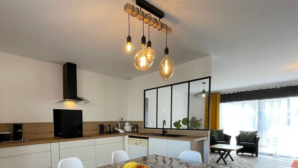 Una cocina moderna con una mesa de madera, sillas blancas y un frutero.