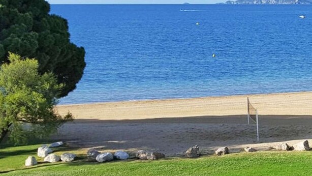 Una playa con vista despejada al mar, un área de césped con rocas y una montaña distante.