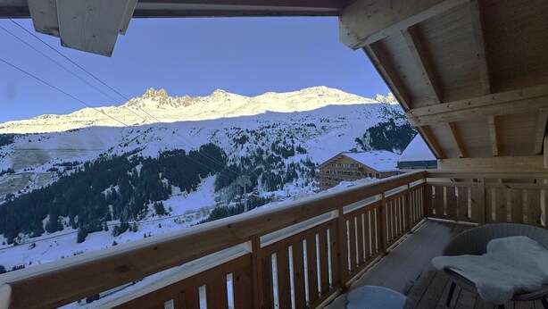 Ein hölzerner Balkon mit Blick auf schneebedeckte Berge und eine Berghütte.