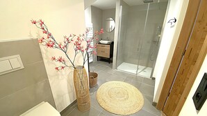 Ein modernes Badezimmer mit Toilette, Waschbecken, Dusche und einer dekorativen Vase mit Zweigen.