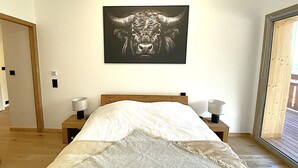 Ein Schlafzimmer mit einem hölzernen Bett, einem Wandbild mit Stier-Motiv, Nachttischlampen und einem großen Fenster.