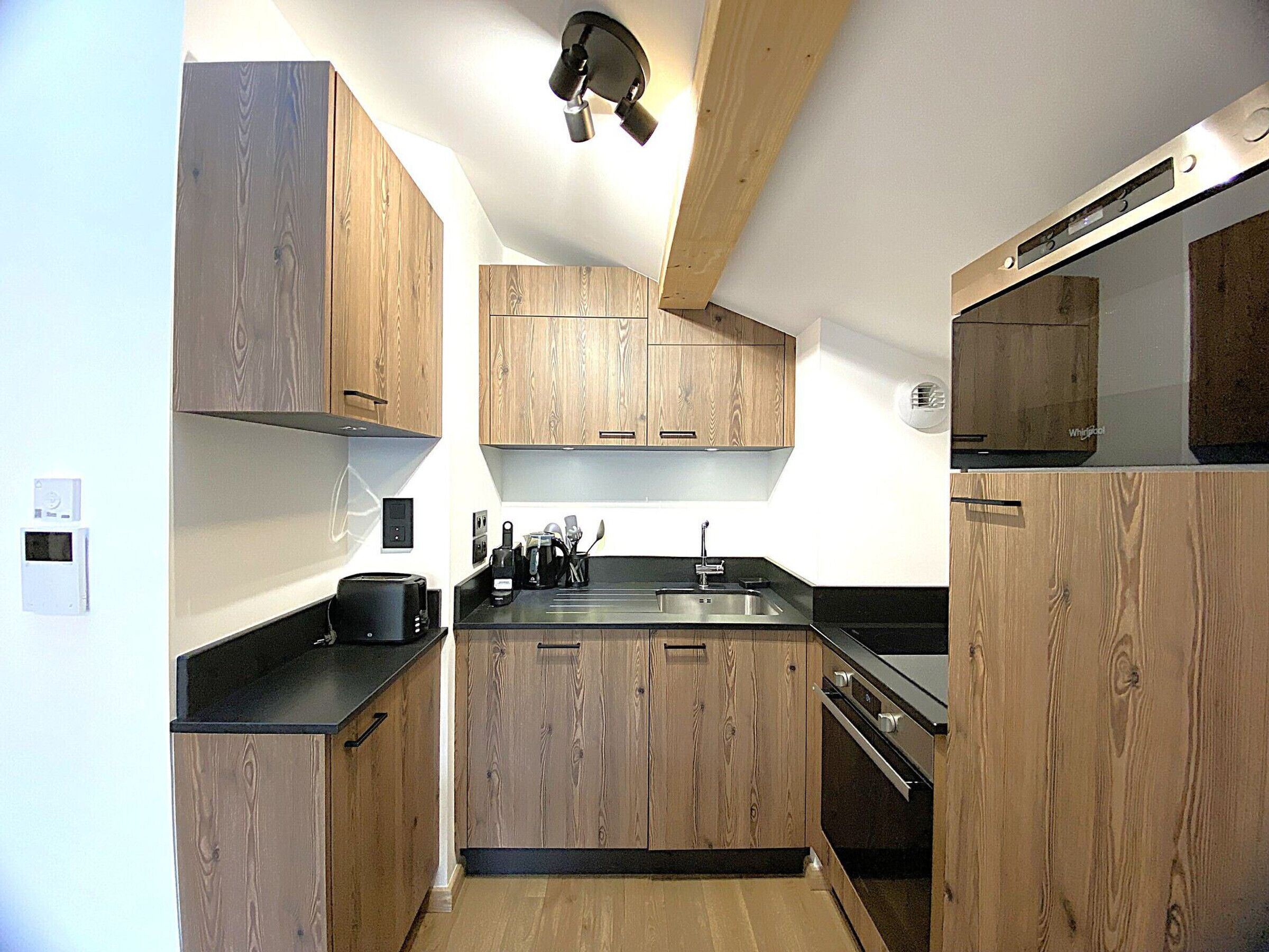 Une cuisine compacte avec des meubles en bois, un plan de travail noir, un four encastré et un four à micro-ondes.