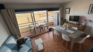 Un salon comprenant un canapé, une table à manger, des chaises, un téléviseur et un balcon offrant une vue sur les immebles.
