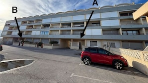 Un immeuble à plusieurs étages doté de balcons, un parking et une voiture rouge garée devant.
