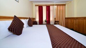 Hotellihuone, jossa on suuri sänky, kaksi tyynyä, puinen pääty ja puinen pöytä, ja josta on näkymä käytävään.