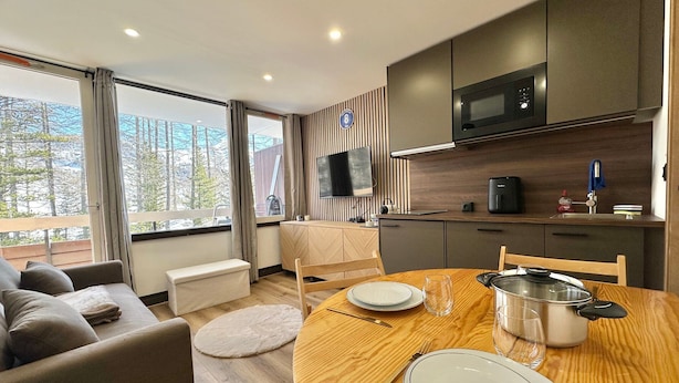 A modern kitchen with a microwave, stove, and sink. There is a dining table with plates and cutlery. A sofa and a small table are in the living area. - Charming renovated studio in the mountains, pets allowed (Vars)