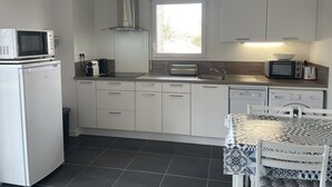 A compact kitchen with white cabinets, a microwave, a toaster, and a sink. There is a window providing natural light and a table with a patterned tablecloth.