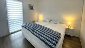 A bedroom with a large bed, two bedside tables with lamps, a window with blinds, and a picture on the wall.