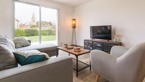 A modern living room with a sofa, armchair, TV, and a floor lamp. - Modern house in Réville, near beach, pets allowed (Reville)