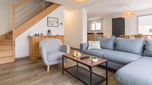 A modern living room with a grey sofa, a wooden coffee table, and a staircase. - Modern house in Réville, near beach, pets allowed (Reville)
