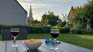 A table with two wine glasses and a bowl of chips, set outdoors with a view of a church and residential buildings. - Modern house in Réville, near beach, pets allowed (Reville)